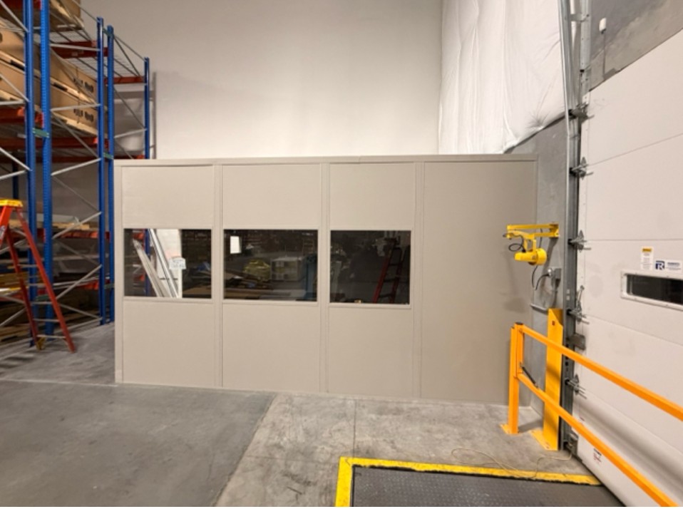 Single-story modular in-plant office with tan walls and viewing windows installed inside warehouse