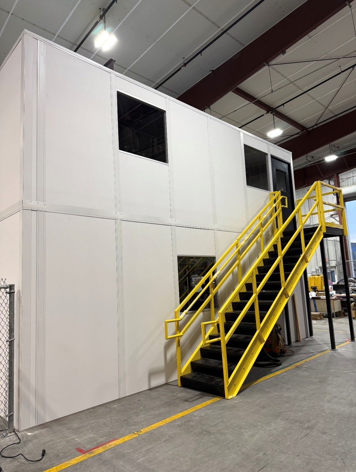 Two-story white modular office with yellow staircase and railings installed inside warehouse for Sodexo